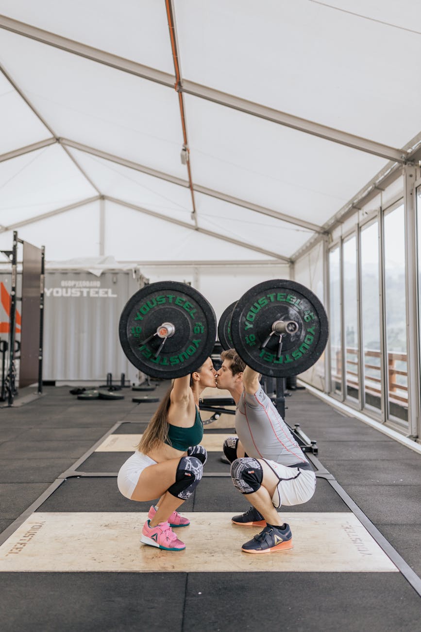 couple kissing while lifting barbells