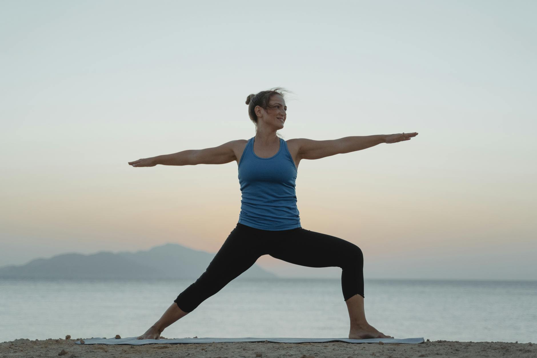 woman in blue tank top and black leggings doing yoga on beach